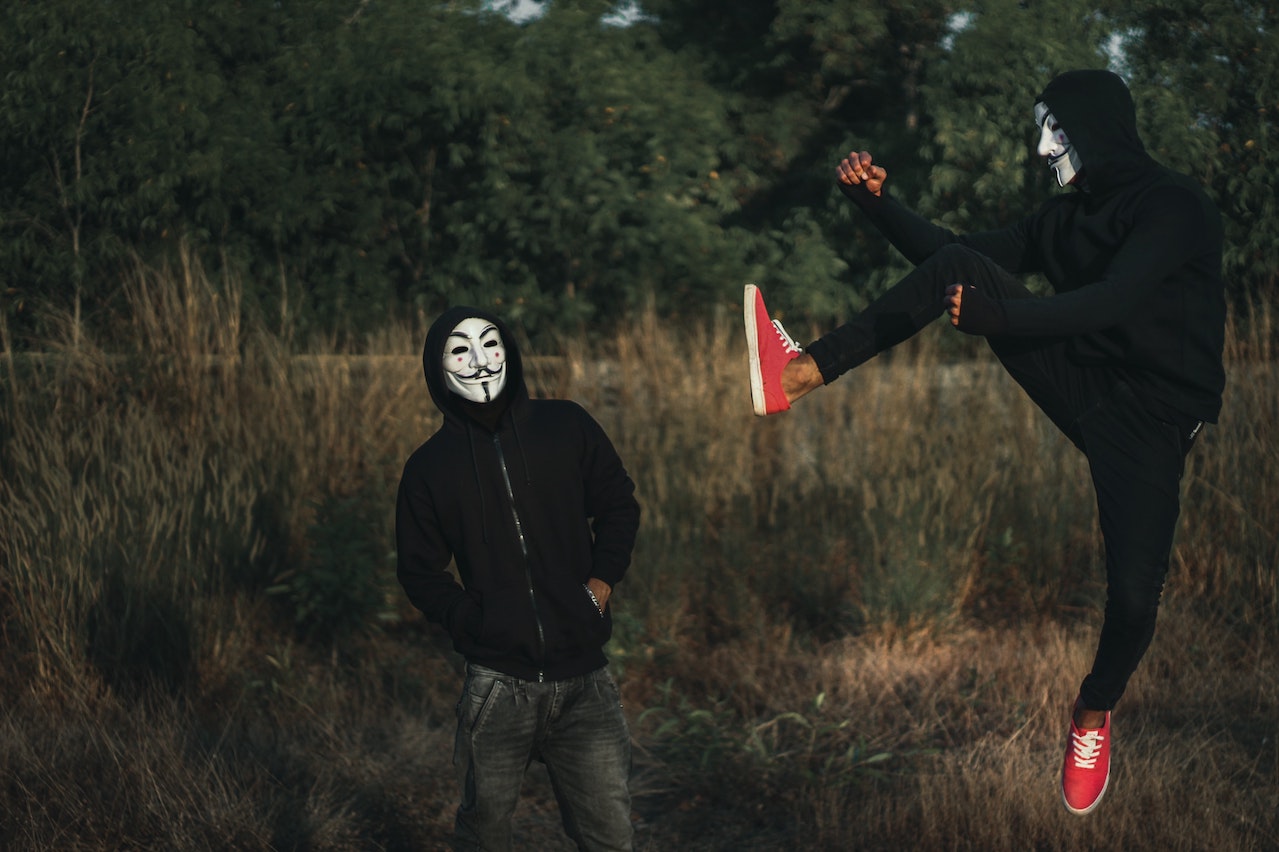 One man wearing the Anonymous hackers group mask kicking another person